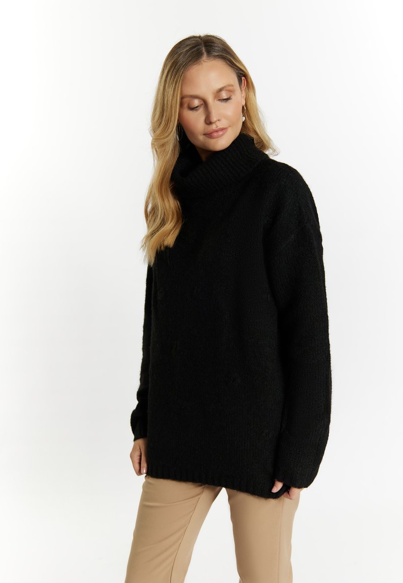Maglione nero oversize lavorato a maglia con colletto alto, tessuto testurizzato e polsini a coste. Abbinato a pantaloni beige.