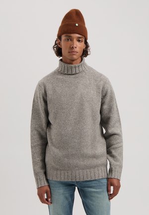 Grijze wollen turtleneck trui met geribbelde halslijn en zoom, voorzien van lange mouwen en een relaxed fit, gedragen met lichtblauwe jeans.