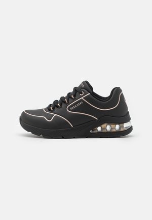 Baskets Skechers noires avec passepoil rose, semelle matelassée avec unité d’air visible, et fermeture à lacets sur fond uni.