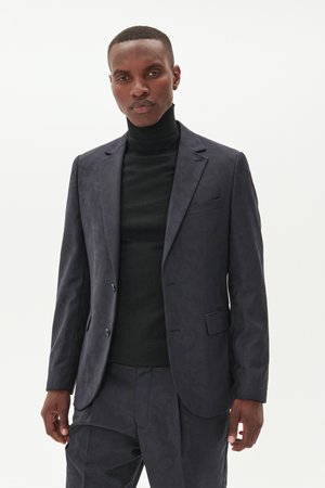 Navy blazer with subtle tonal pattern, single-breasted design, notched lapels, and two silver buttons. Worn over a black turtleneck.