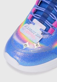 Basket de sport en synthétique bleu avec paillettes, accents arc-en-ciel, quincaillerie rose et une étiquette indiquant "JE LUMINE ! AVEC BOUTON MARCHE/ARRÊT."