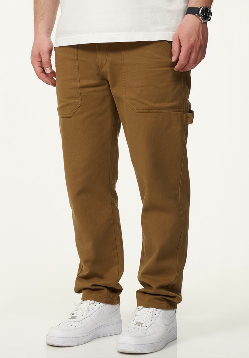 Brown cargo pants made of cotton blend fabric, featuring front patch pockets and a side cargo pocket, paired with white sneakers.