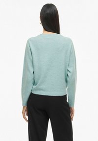 Gaiši tirkīza džemperis ar apaļu kaklu, garām piedurknēm un īsu piegriezumu. Audums šķiet mīksts un gludas tekstūras.