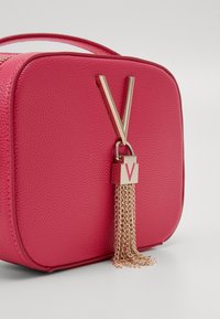 Pink textured handbag with a rectangular shape, featuring a gold tassel and hardware detailing, including a prominent "V" emblem.