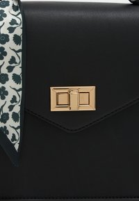 Μαύρη δερμάτινη τσάντα χειρός με κλείσιμο από χρυσόχρωμο υλικό και αξεσουάρ φουλάρι με floral σχέδιο προσαρτημένο στο πλάι. Λείο υλικό.