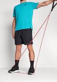 Turkos kortärmad träningsskjorta med geometriskt mönster, svarta kortbyxor och svarta sneakers med vita sulor; röd motståndsband i bruk.