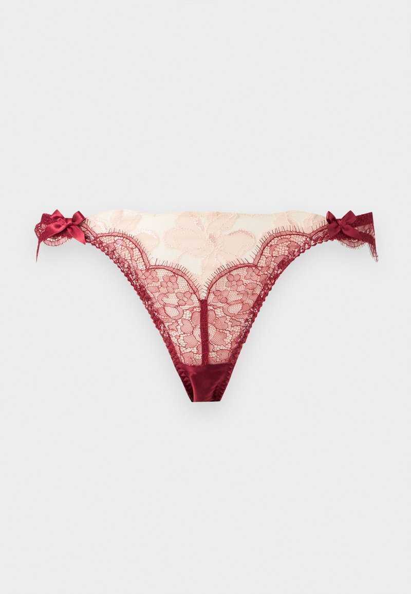 String en filet floral beige transparent et dentelle rouge avec nœuds en satin sur chaque hanche, présenté sur un fond clair uni.