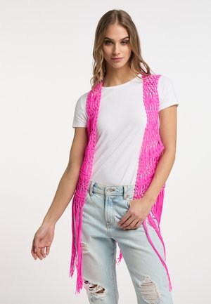 Vest tricotat roz aprins, cu detalii de franjuri, purtat peste un tricou alb, stratificat cu blugi ușor rupți de culoare albastră deschisă. Hardware minim vizibil.
