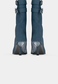 Denim ankelstøvler i mørkeblå med sølvspenne og spiss tå. Har stilettosåle og teksturert overdel med sømdetaljer.