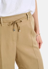 Beige široké kalhoty s elasticitou v pase, předními kapsami a hladkým, lehkým materiálem. Stříbrné detaily na šňůrce.