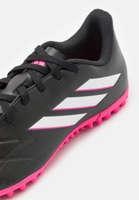 Le scarpe da calcio nere presentano una tomaia testurizzata, suola rosa e strisce bianche. Progettate per la trazione, con un sistema di chiusura con lacci per una vestibilità sicura.