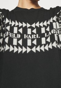 Czarny sweter dziany z geometrycznym wzorem białych trójkątów i napisem, z prążkowanym, okrągłym dekoltem.