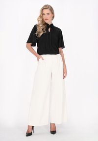 Blus hitam dengan dasi leher dan lengan pendek, dipadukan dengan celana putih berpinggang tinggi dan lebar serta sepatu hak tinggi berwarna hitam.