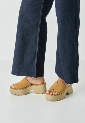 Braune Plateausandalen aus Veloursleder mit dicker beigefarbener Gummisohle. Offenes Zehendesign mit breitem Riemen über dem Fuß und gesteppten Details.