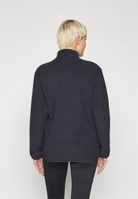 Tumesinine fleece-pullover kõrge kaelusega, pika varruka ja lõdva lõikega. Pehme tekstuur ja ümmargune hem taga.