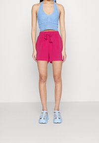 Svetle modrý pletený top na krk, růžové kraťasy s opaskem a modré sandály s otevřenou špičkou a detailem pásků.