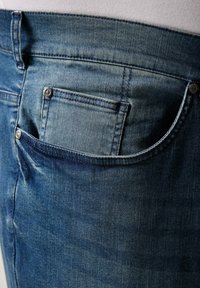 Jeans i denim med en mellanblå tvätt och en synlig bakficka. Funktioner inkluderar silverdetaljer, synlig sömnad och en lätt blekning.
