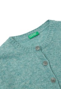 Błękitny sweter z dzianiny z okrągłym dekoltem, trzema szarymi guzikami i widoczną zieloną metką United Colors of Benetton.