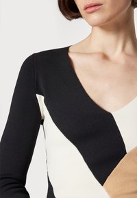Striktop med V-hals og lange ærmer. Farveblokeret design med sektioner i sort, hvid og beige. Tekstil med tekstur.