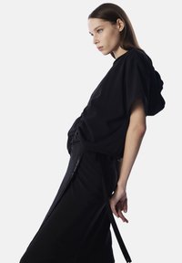 Haut noir à manches courtes avec une coupe décontractée et une capuche, associé à une jupe noire avec une fermeture éclair sur le côté et des liens ajustables. Texture lisse.