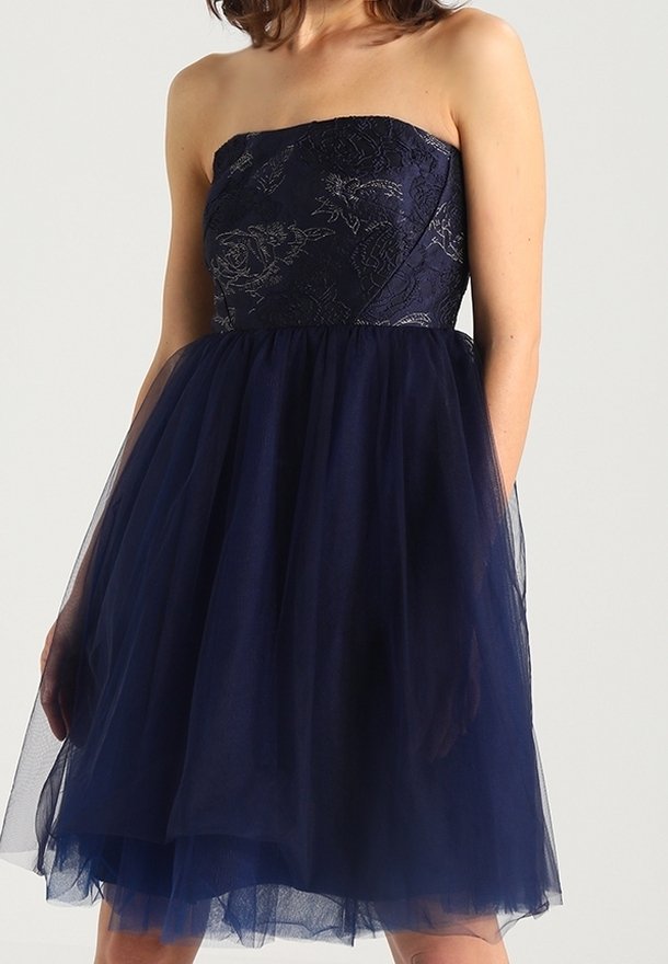 Axelös klänning i marinblått; har en spetsöverdel med blommönster och en lager på lager av tyllkjol. Mjuk textur och knälång design.