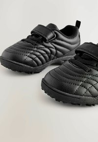Zwarte sportieve schoenen met een gestructureerde leren bovenkant met gestikte patronen, een klittenbandsluiting en rubberen zolen met tractiestuds.