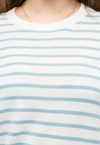 Κοντινό πλάνο ενός ατόμου που φοράει άσπρο και ανοιχτό μπλε οριζόντια ριγέ πουκάμισο και λεπτή χρυσή αλυσίδα στο λαιμό.