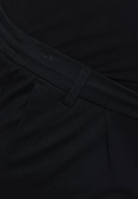 Zwarte broek met een gladde stofstructuur, een platte tailleband en vóór plooien, die zorgt voor een getailleerde pasvorm.