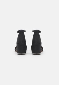Black heeled sandals with a smooth texture, adjustable ankle straps, and a block heel featuring a metallic accent around the base.