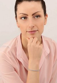 Bracciale d'argento con accenti circolari, indossato su un polso. Una camicia leggera di colore rosa chiaro è parzialmente visibile. Texture lisce e design minimalista.