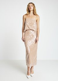 Sequin dress in blush pink with spaghetti straps, fitted silhouette, and a midi length. Smooth texture with shiny accents, paired with white heels.