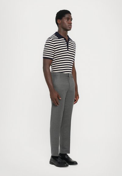 Randig polo tröja i mörk marinblå och krämfärgad färg, kortärmad; grå skräddarsydd byxor; svarta skor. Minimalistisk, åtsittande design.