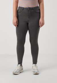 Vaqueros de mezclilla gris con un corte ajustado, que cuentan con bolsillos frontales y un cierre de botón. Combinados con zapatillas deportivas plateadas y blancas.