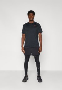 Strój sportowy Nike składający się z czarnej koszulki z krótkim rękawem z czerwonym logo, czarnych spodenek oraz czarnych legginsów z białym logo. Buty sportowe są czarne.