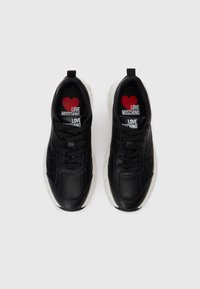 Melni ādas sporta apavi ar baltiem zolemi, melnām šņorēm un sarkanu sirdeles zīmolu "Love Moschino" katra apava iekšpusē.