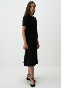 Zwart, getextureerd gebreid T-shirt met korte mouwen en een losse pasvorm, gecombineerd met een bijpassende zwarte rok tot de knie en platte enkelsandalen.