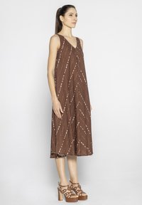 Brązowa sukienka bez rękawów z dekoltem w szpic, ozdobiona białymi, ukośnymi paskami. Uzupełniona masywnymi, brązowymi sandałami na platformie. Gładka tekstura.