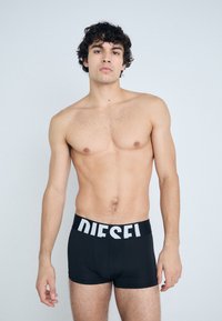 Fekete boxer alsónadrág, merész fehér "DIESEL" logóval a rugalmas deréknál. Sim szó, rugalmas anyag, amely a testhez simul.