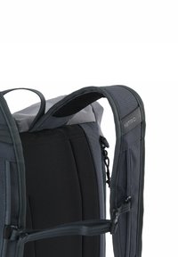 Sac à dos noir et gris avec bretelles rembourrées, tissu texturé et une poignée supérieure. Comprend un détail avec logo et des poches latérales.