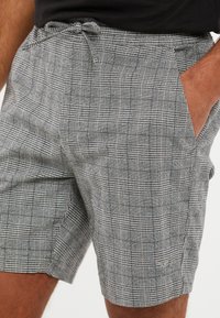 Pantalones cortos de cuadros grises, confeccionados en tejido ligero, con una cinturilla elástica y cordón, bolsillos laterales y un corte relajado.