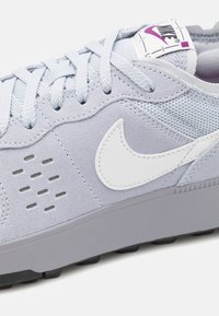 Ljusgrå sneaker i mesh och mocka, rund tå, vit Nike-logotyp, texturerade accenter och platt grå gummisula.
