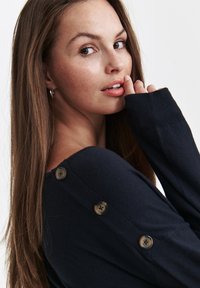 Granatowy sweter dzianinowy o luźnym kroju, z dużymi guzikami na ramieniu i prążkowanymi mankietami. Miękka tekstura i swobodny design.