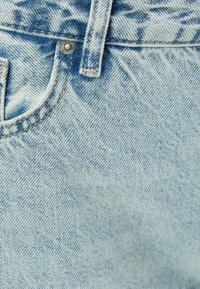 Ljusblå denimtyg med en subtil tvätteffekt, som har en metallknapp och sömnadsdetaljer längs fickan och midjebandet.