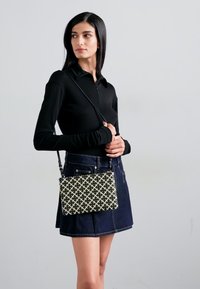 Top nero a maniche lunghe, gonna di jeans, tiene una borsa rettangolare con un motivo geometrico in bianco e nero e una tracolla.