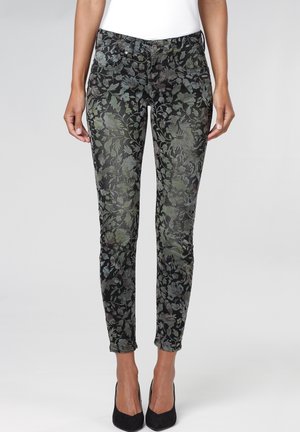 Zwarte slim-fit jeans met groen en grijs bloemmotief, gedragen met zwarte hakken en een wit topje, getoond van taille tot enkels.