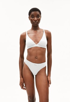 Femme debout, de face, portant un soutien-gorge triangle blanc et un slip taille haute sur un fond blanc uni.