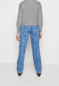 Blaue Denim-Jeans mit einem geometrischen Karomuster, geradem Bein und Gesäßtaschen. Kombiniert mit einem strukturierten grauen Strickpullover.