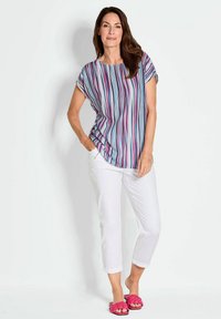 Kurzarmtop mit vertikalen Streifen in Blau, Pink und Weiß, kombiniert mit weißen Knöchelhosen und rosa geflochtenen Rutsch-Sandalen.