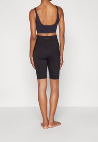 Czarna sportowa bielizna na przestrzeń z szerokimi ramiączkami, w połączeniu z czarnymi szortami rowerowymi o podwyższonym stanie. Materiał wydaje się gładki i matowy.
