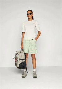 Lys grå kortermet t-skjorte, myntegrønne cargo-shorts, grå tursko og en ryggsekk med flerfargede detaljer. Solbriller brukt.